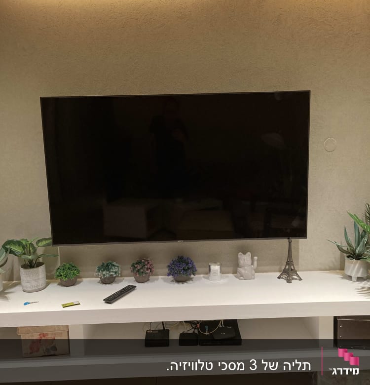 טלוויזיה תלויה על קיר עם שלט על מדף